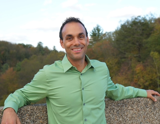 A man in a green shirt leaning against a stone wall